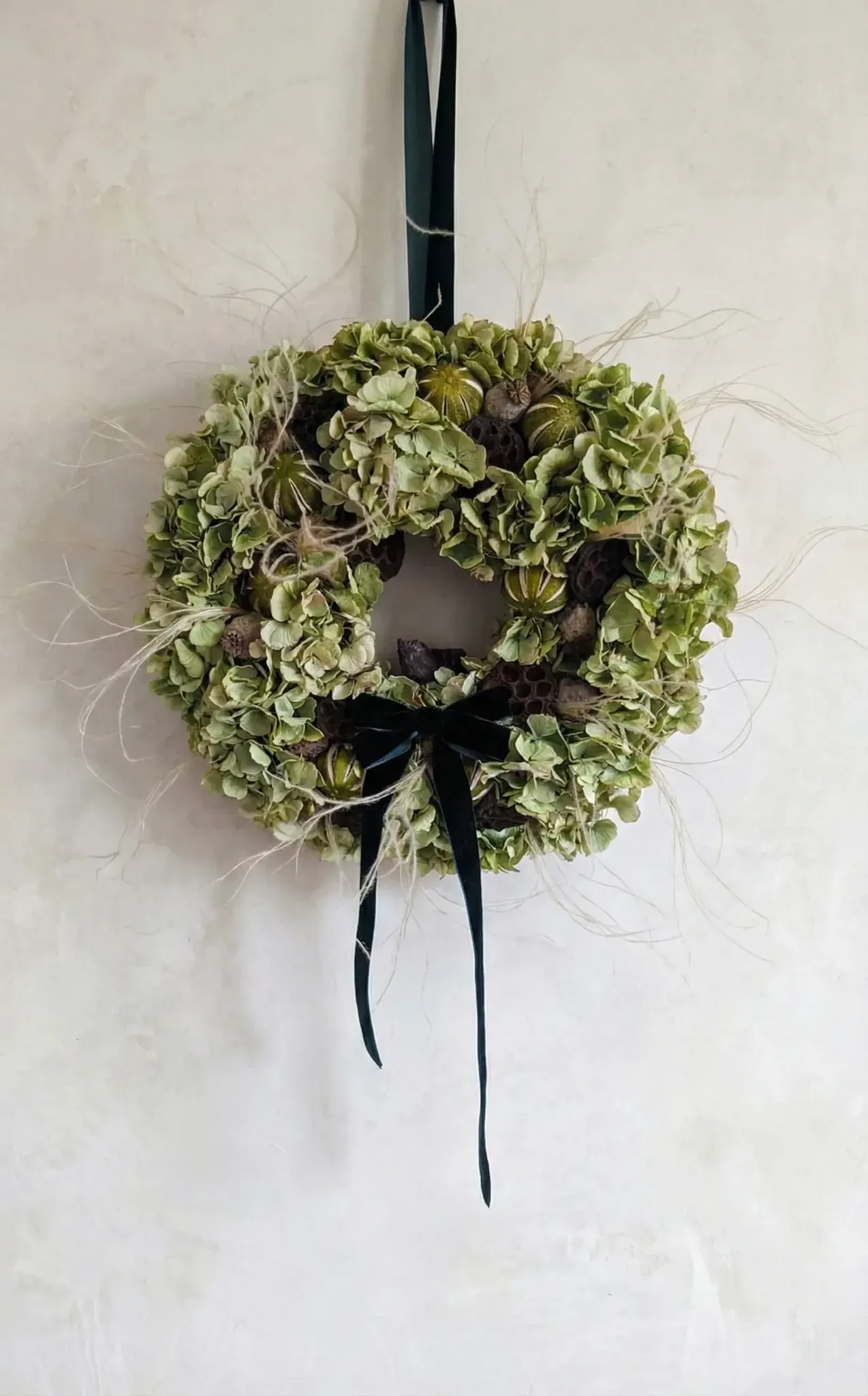 Natural green hydrangea Christmas wreath with lotus pods, poppy pods and preserved green oranges with velvet bow handmade in London